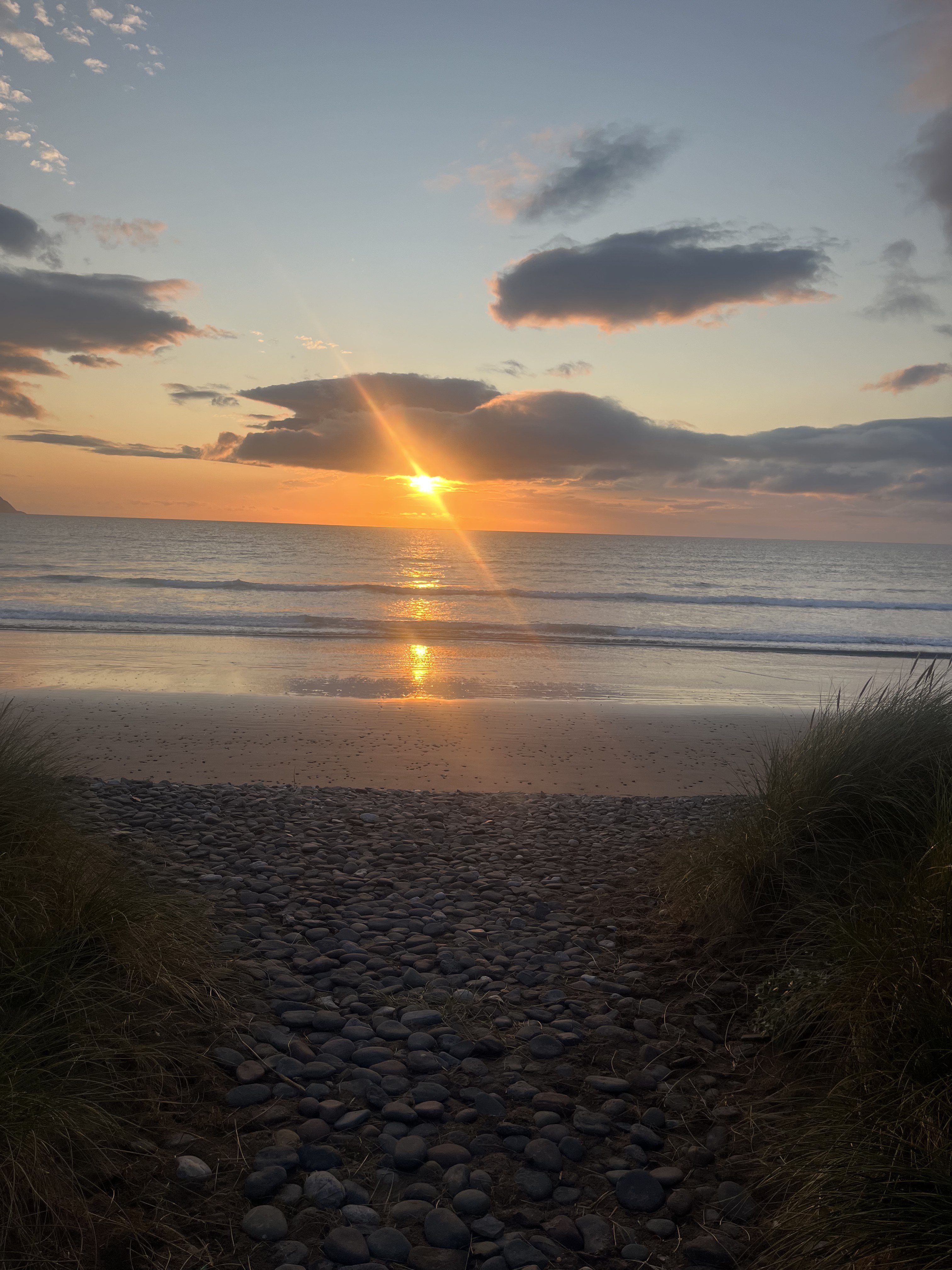 Sunset over Castlegregory beach with pebbled path through the dunes